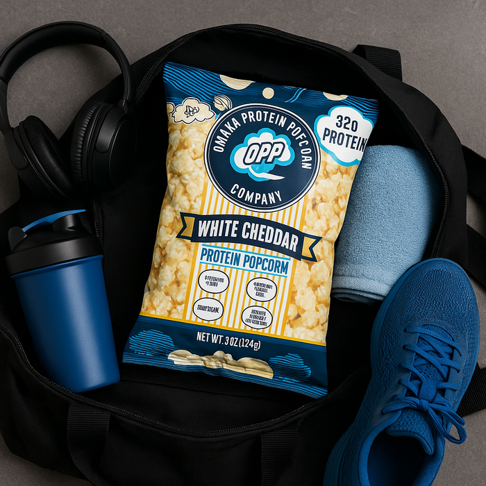 A gym locker or open gym bag with all the essentials (shaker, towel, headphones, trainers)—and a few Omaha Protein Popcorn bags peeking out. Maybe one bag half-open with popcorn spilling out onto a yoga mat.