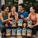 Square image of a group of friends in gym clothes enjoying Omaha Protein Popcorn after a workout outside a fitness studio. Seven authentic popcorn bags sit open and upright in the center, with hands reaching for popcorn. The vibe is fresh, active, and fun, with clear branding on every bag.