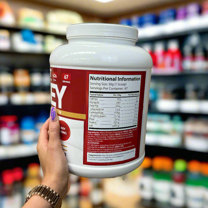 MYSUPPLEMENTSHOP’s Abbie, sporting branded purple nails, holding a tub of whey protein powder in-store, showcasing the nutritional information label with 22g protein per scoop and 67 servings clearly visible.